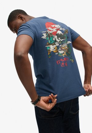 Marineblauwe katoenen t-shirt met een kleurrijke grafische print op de achterkant, waarop figuren met wolken en een draak worden afgebeeld, plus rode tekstaccenten.