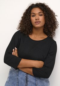 Haut noir à manches longues avec un col rond, fabriqué en tissu doux et léger. Coupe légèrement ample, associé à une jupe en denim bleue.