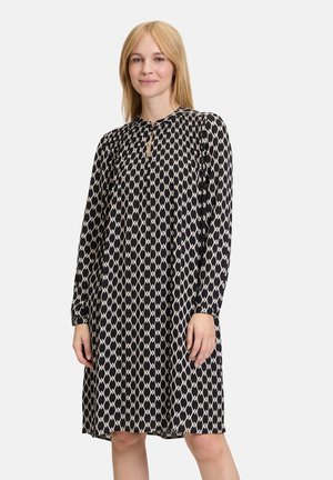 Schwarzes und cremefarbenes, gemustertes langärmliges Kleid mit schlüssellochförmigem Ausschnitt, fließendem Schnitt und knie-langer Saum. Weicher Stoff mit glatter Textur.