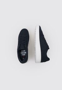 Baskets en daim noires avec semelles en caoutchouc blanches. Présentent un bout arrondi, un laçage à l'avant et un texte à l'intérieur indiquant "PARCE QU'IL N'Y A PAS DE PLANÈTE."