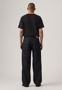Jeans de mezclilla negra con un corte relajado, que cuentan con un parche de piel marrón en la parte trasera, dos bolsillos y un diseño de pierna recta.