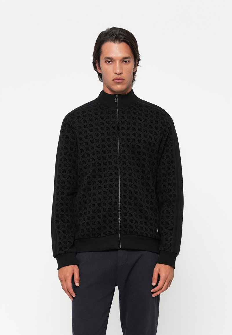 Zwarte zip-up jas met een patroontextuur. Heeft een geribbelde kraag, manchetten en zoom. Zijstrepen voegen detail toe. Gladde stofafwerking.