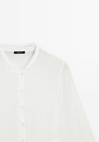 Chemise blanche à manches longues boutonnée, col rond, tissu léger et étiquette "Massimo Dutti" à l'intérieur de l'encolure.