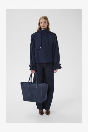 Navy cropped jacket with double-breasted buttons, matching navy suede tote bag, dark denim high-waisted pants, and pointed brown heels.