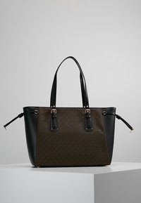 Bruine en zwarte totebag gemaakt van synthetisch materiaal, met gouden hardwareaccenten, dubbele handvatten en een geometrisch patroon aan de voorkant.