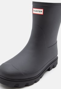 Black rubber rain boot with a textured finish, a sturdy sole featuring deep grooves, and a HUNTER logo on a red and white label.