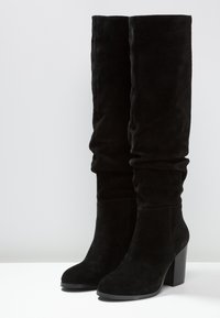 Bottes hautes jusqu'au genou en daim noir avec un design décontracté, bout arrondi et talon haut épais. Texture lisse, ornementation minimale.