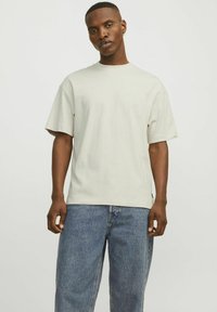 Beige rövid ujjú póló, kerek nyakkivágással, világoskék, laza szabású farmernadrággal párosítva. Az anyag simának tűnik, minimalista dizájnnal.