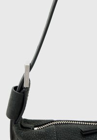 Sort textured læderhåndtaske med en glat rem, sølv hardware og lynlås-lukning. Bemærkelsesværdige detaljer inkluderer et præget logo og minimalistisk design.
