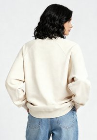 Sweat-shirt de couleur crème, coupe décontractée, avec manches raglan et poignets côtelés. Tissu doux à la texture lisse.