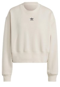 Klippt beige sweatshirt i mjukt tyg, med rund halsringning och en liten svart Adidas-logotyp på bröstet. Långa ärmar med ribbade manschetter.