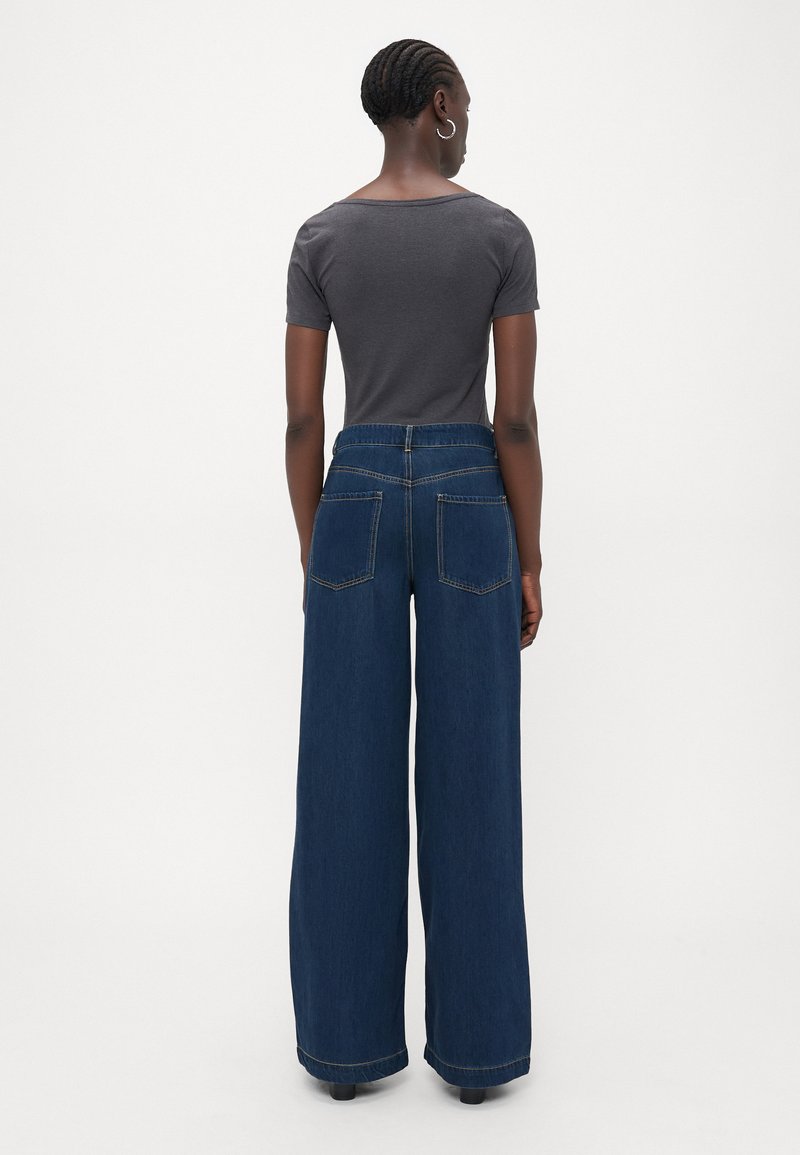 Szerokie, ciemnoniebieskie dżinsy z wysokim stanem, z dwiema tylnymi kieszeniami i wykończonym dołem, połączone z dopasowanym, szarym topem z krótkim rękawem.