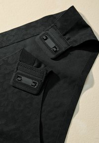 Black fabric featuring a subtle embossed pattern, with two adjustable straps and black clasps, offering a textured, sleek design.