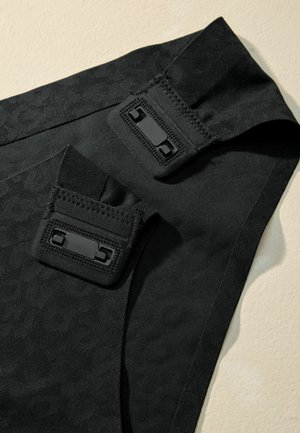 Černá tkanina s jemným embosovaným vzorem, se dvěma nastavitelnými popruhy a černými sponami, nabízející texturovaný, elegantní design.