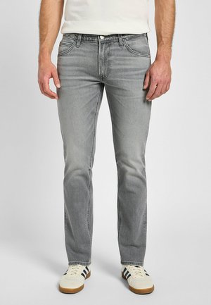 Szare dżinsy o dopasowanym kroju, z pięcioma kieszeniami, lekkim przetarciem i kontrastowym przeszyciem; zestawione z białymi sneakersami z czarnymi akcentami.