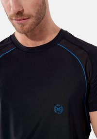 Svart idrottströja med blå detaljer, rund halsringning och mesh-paneler på axlarna. Logotypen visas på bröstet.