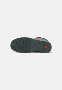 Suela de bota de goma verde con una superficie texturizada, que presenta un acento circular rojo cerca del talón y un diseño de banda de rodadura para mayor agarre.