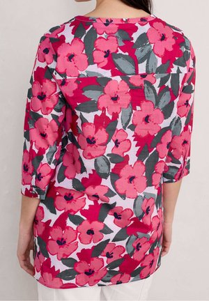 Túnica floral con mangas tres cuartos, que presenta grandes flores rosas, hojas verde oscuro y un fondo claro, confeccionada con una tela ligera.