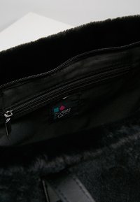 Černý umělý kožich uvnitř tašky s kapsou na zip a malou značkovou nálepkou s geometrickým designem. Měkká textura, funkční design.