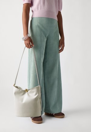 Lys rosa strikket genser, mintgrønne corduroy bukser med vide ben, klar armbånd, kremfarget skulderveske med gulldetaljer, og brune sko.