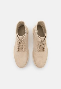 Zapatos de ante beige con punta redonda, que presentan un diseño de cordones y cremallera lateral. Textura suave con una suela cosida.