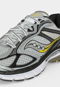 Γκρι και λευκό παπούτσι τρεξίματος Saucony με κίτρινες λεπτομέρειες και λευκά κορδόνια, που δείχνει διαπνέον δίχτυ και λεπτομέρειες με επένδυση στην σόλα.