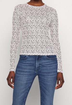 Person wearing fitted long-sleeve top with black and white repeating "HOU" pattern paired with blue denim jeans, standing against a plain background.