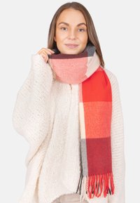 Écharpe à carreaux rouge et gris avec des bords frangés, faite de tissu doux, enroulée autour du cou, présentée sur un fond clair.