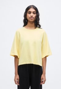 Haut jaune à manches courtes et coupe ample en tissu tricoté texturé, avec un col rond et un ourlet raccourci, associé à un pantalon noir.