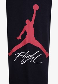 Silueta basketbalisty skákajícího s nataženýma rukama, držícího míč, nad slovem „Flight“ ve stylizovaném písmu na tmavé látce.