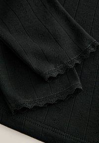 Schwarzer Strickstoff mit gerippter Textur, der mit gewellten Spitzenkanten und dezenten floralen Mustern im gesamten Material versehen ist.