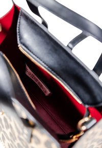 Interno della borsa a tracolla nera e leopardata, con rivestimento in tessuto rosso, cerniera dorata e un'etichetta. Tessuto liscio con design strutturato.