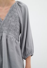 Hallharjas pluus V-kaeluse, rinda smockitud ja elastsete mansettidega balloonvarrukatega, tehtud kergest ja struktuurilisest kangast.