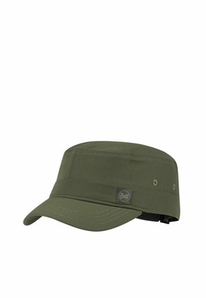 Mujer con cabello largo trenzado que lleva una gorra verde oliva y una camiseta verde oliva a juego, mirando hacia su izquierda sobre un fondo blanco.