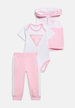 Ensemble bébé trois pièces avec body à manches courtes rose et blanc, gilet à capuche sans manches, et pantalon assorti avec logo Guess.
