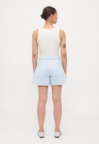 Shorts rayés bleu clair à taille haute, avec des poches arrière et une texture lisse, associés à un haut sans manches blanc.