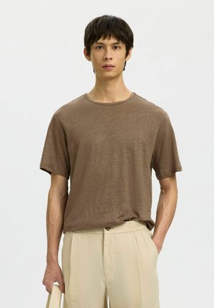 T-shirt marrone a maniche corte in tessuto morbido e strutturato; scollo rotondo, vestibilità rilassata, abbinato a pantaloni chiari e ampi.