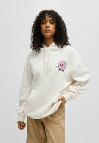 Hoodie beige clair en tissu doux avec une poche kangourou, présentant un graphique de donut rose sur le côté gauche et un cordon de serrage pour la capuche.