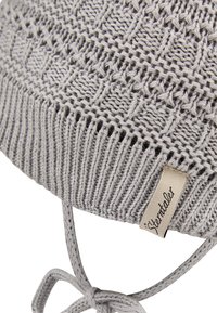 Knit hat in light gray, featuring a textured pattern and braided ties. Includes a small tag with the brand name stitched onto the side.