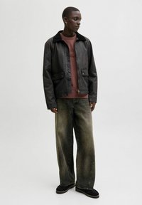 Black, cropped jacket with a faux fur collar, featuring buttoned pockets, layered over a maroon sweatshirt and wide-legged faded jeans.