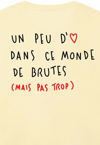 Text on a light yellow shirt reads: "Un peu d❤️ dans ce monde de brutes (mais pas trop)." The heart is highlighted in red.
