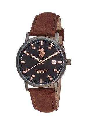 Round black wristwatch with brown leather strap, gold hour markers, three hands, date window at three o'clock, and U.S. Polo Assn. logo on face.
