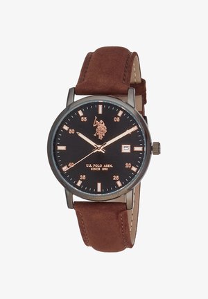 Montre-bracelet ronde noire avec bracelet en cuir marron, index dorés, trois aiguilles, guichet date à trois heures et logo U.S. Polo Assn. sur le cadran.