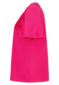 Blouse à manches courtes rose vif avec des appliqués de rose en tissu sur le devant, présentée de profil sur fond blanc.