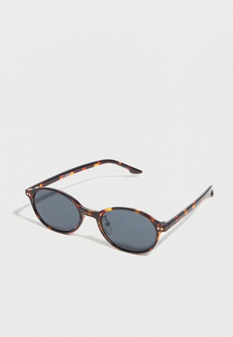 Στρογγυλά γυαλιά ηλίου με σκοτεινούς φακούς και λεπτό πλαστικό πλαίσιο με μοτίβο χελώνας σε λευκό φόντο.