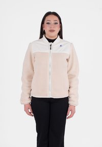Fleecejas in beige met een wit paneel op de schouders, ritssluiting en geribbelde manchetten; met een klein logo aan de linkerbovenzijde.