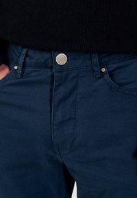 Chino in cotone blu navy con una trama liscia, caratterizzati da una chiusura con bottone argento, passanti per cintura e tasche laterali.
