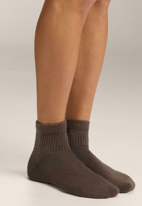 Személy barna boka fölé érő bord ázott zokniban, egy sima, világos színű felületen áll, lábak a vádli közepétől lefelé láthatóak.