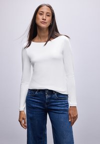 Hvid bluse med lange ærmer og rund halsudsk�æring, parret med blå vide jeans. Stof looks glat og tætsiddende.