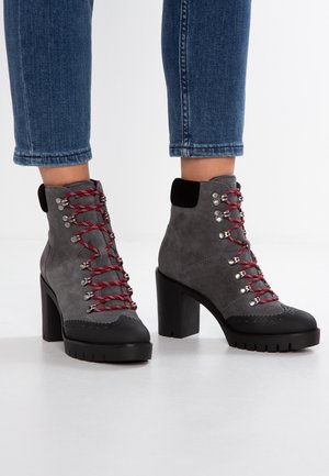 Bottes montantes en daim gris à lacets avec bouts noirs, talons hauts épais, lacets rouges, portées avec un jean bleu raccourci.